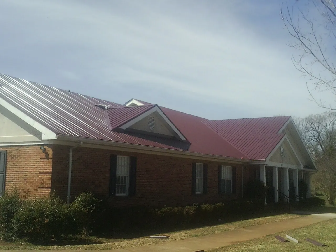 Red metal roof with gabled entries on a long brick building, from a Hail Damage Roof Repair job in Altamont