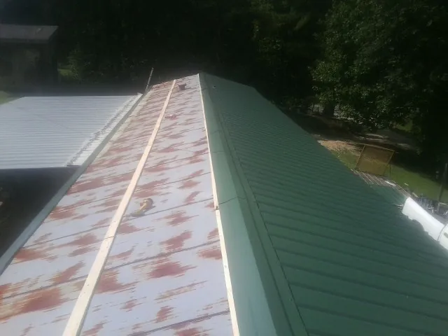Old rusted panels beside newly installed green metal roofing — Wind Damage Roof Repair by Roofing Brothers in Altamont